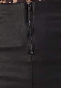 Svart zippered plagg med en slät yta, med en framträdande dragkedjedetalj på ena sidan som sträcker sig vertikalt längs tyget.