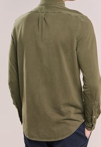 Camicia a maniche lunghe verde oliva con colletto a punta, dettaglio con piega posteriore e polsini con bottoni. Realizzata in morbido cotone.