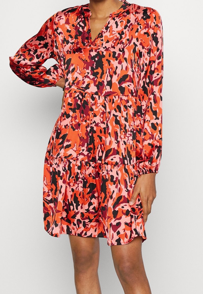 Femme portant une robe à manches longues avec un motif abstrait coloré rouge, rose et noir, avec un col en V et une jupe à volants.