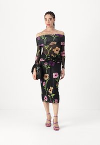 Abito nero con fiori, design off-shoulder, maniche lunghe trasparenti e fantasie floreali colorate. Tacchi viola con cinturini completano il look.