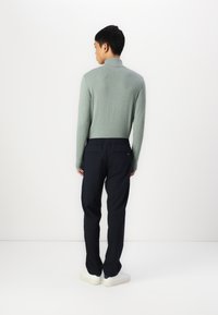 Light green fitted long-sleeve top, paired with dark navy elastic-waist pants, worn with white sneakers on a neutral backdrop.