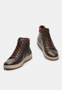 Brown leather high-top boots with padded collar, brown laces, and beige textured sole. Features metal eyelets and smooth, polished finish.