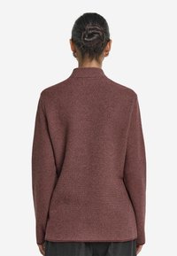 Mörkröd tröja med ett texturerat fiskbensmönster, långa ärmar och krage. Designad med en något lös passform och sidslitsar vid fållen.