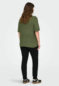 Alyvuogių žalios spalvos trumpomis rankovėmis palaidinė, laisvas kirpimas, tekstūrinis mezgimo audinys; derinama su juodomis kelnėmis ir juodai baltomis sportbačiais.