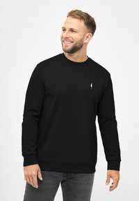 Sudadera negra de cuello redondo hecha de tela suave con mangas largas, que presenta un pequeño logo de árbol blanco en el lado izquierdo del pecho y puños acanalados.