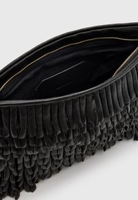 Mustasta nahasta valmistettu clutch-laukku, jossa on fringed-tyyppisiä yksityiskohtia. Sisäosassa on vuorattu osasto ja pieni tasku. Kultainen vetoketju.