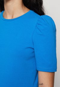 Blå kortärmad t-shirt med rund halsringning och rynkade axeldetaljer. Mjuk tyg med slät textur och lättviktsdesign.