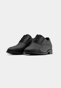 Chaussures habillées en cuir noir présentant une texture lisse, un bout arrondi, des coutures surélevées et un design classique à lacets avec un talon bas.