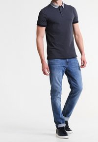 Polo marine à manches courtes avec une texture à motifs et un col contrastant gris, associé à un jean bleu clair et des baskets noires.