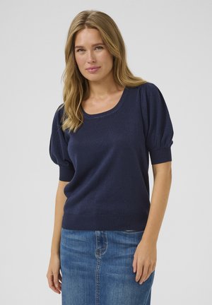 Pull en maille bleu marine avec un décolleté rond et des manches courtes bouffantes. Présente une finition texturée et un ourlet côtelé, associé à une jupe en denim.