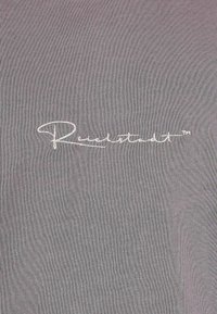 Tessuto grigio con una sottile trama e un logo bianco ricamato, "Reutstadt™", posizionato nell'angolo in basso a destra.