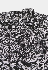 Tissu noir avec des motifs floraux blancs, doté d'une large ceinture, d'une boucle et de pliages pour la texture et la forme.