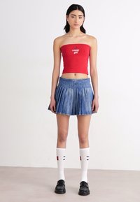 Rdeča brezramna kratka majica s tekstom "tommy girl", v kombinaciji s plisirano jeans krilo. Dodatki vključujejo bele nogavice do kolen in črne čevlje.