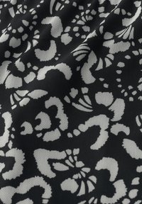 Schwarzer Stoff mit einem weißen abstrakten Blumenmuster, das verschiedene Formen, Texturen und Größen aufweist, entworfen mit einem atmungsaktiven Mesh-Qualität.