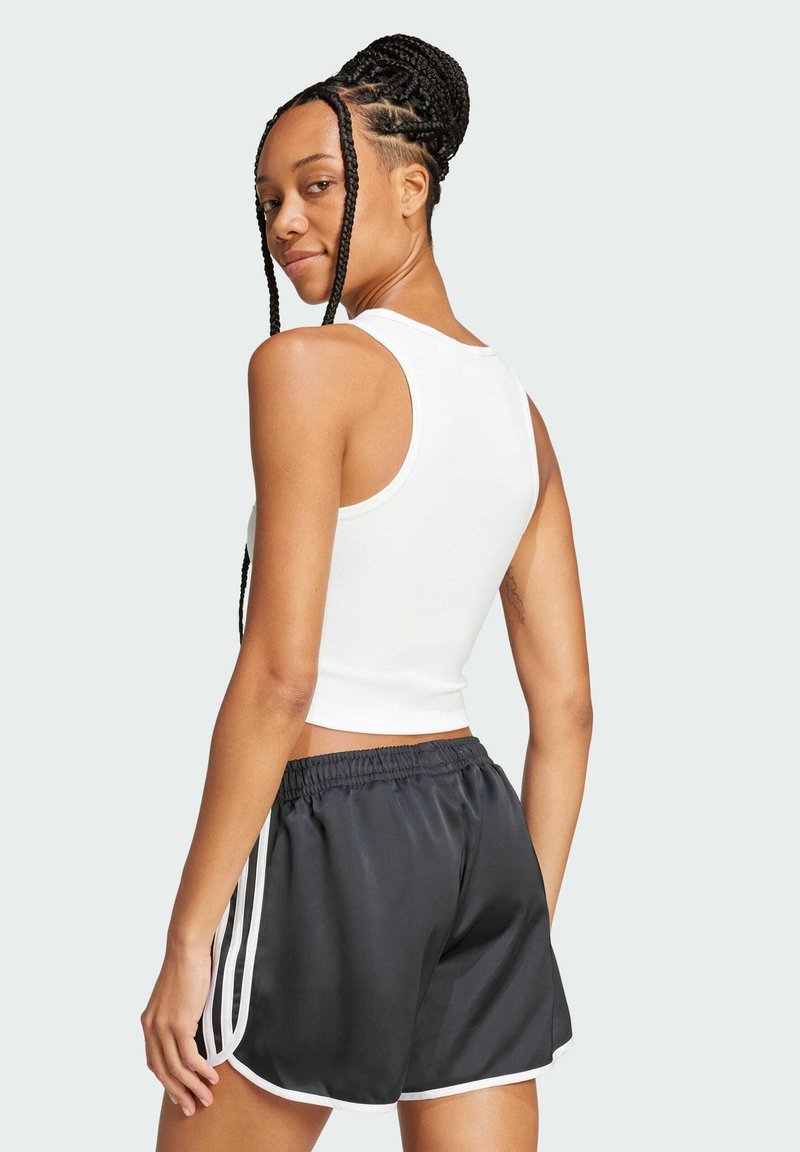 Vit ribbad kort tanktop paired med svarta sportshorts med vita sidostripor. Slät textur, figurnära design.