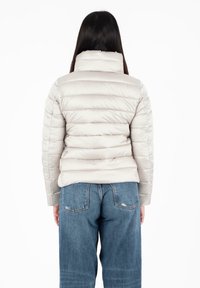 Lichtbeige pufferjack met een hoge kraag, horizontaal gestikt ontwerp en een gladde textuur, gecombineerd met blauwe high-waisted jeans.
