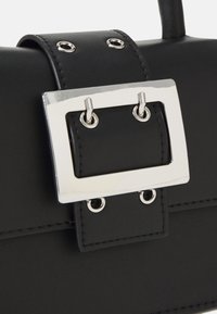 Gros plan sur un sac en cuir noir avec une grande boucle rectangulaire en argent et des œillets sur la sangle.