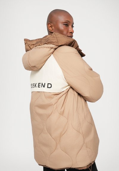 Casaco puffer acolchoado bege com um painel branco em contraste apresentando o texto "WEEKEND". O capuz é castanho e o design inclui uma bainha ajustada.