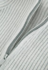 Grauer Strickpullover mit vertikaler Rippenstruktur; verfügt über einen silbernen Reißverschluss, weichen Stoff und einen leichten Glanz.