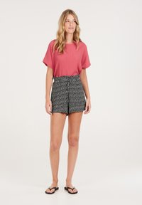 Haut rouge texturé à manches courtes associé à un short taille haute noir à motifs et des tongs noires. Tenue décontractée d'été.