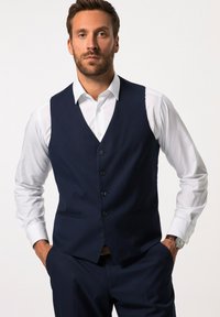Marineblaues Weste mit glatter Textur, V-Ausschnitt, fünf Knöpfen und zwei vorderen Taschen, kombiniert mit einem weißen Hemd.