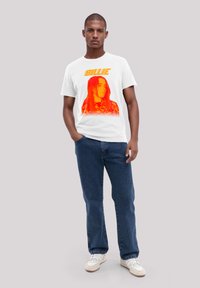 White t-shirt featuring an orange and red graphic of a person's face and the text "BILLIE" above. Worn with blue jeans and white sneakers.
