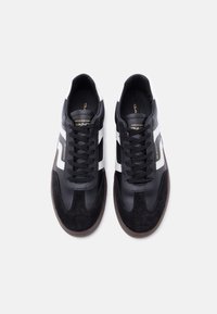 Μαύρα αθλητικά παπούτσια από δέρμα και σουέτ, με λευκές ρίγες, στρογγυλά κορδόνια και υφασμένη λαστιχένια σόλα. Χρυσές λεπτομέρειες λογότυπου στη γλώσσα.