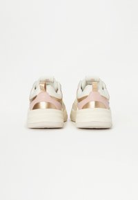 Ténis com um upper de tecido branco, detalhes metálicos em rosa e dourado, uma sola branca robusta e um pequeno tab para facilitar o calçar.