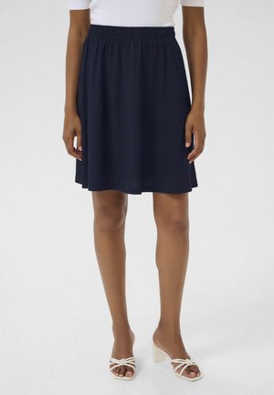 Jupe patineuse bleu marine en tissu texturé, dotée d'une taille élastique. Associée à des talons blancs à lanières et affichant une finition lisse.