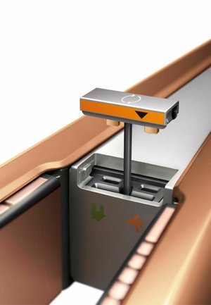 Stampante per etichette metalliche regolabile per bagagli con parti arancioni e grigie, montata su un sistema a binario all'interno di un vano bagagli.