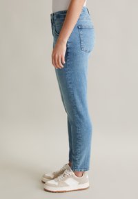 Jasnoniebieskie dżinsy o slim fit, z wysokim stanem, delikatnym efektem wypłowienia i klasycznym pięciopocketowym fasonem. W połączeniu z beżowymi sneakersami.