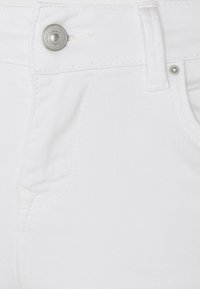 Tejido de denim blanco que presenta un primer plano de la cintura con un botón metálico y un detalle de costura superior. Textura suave y diseño minimalista.