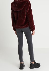 Burgundowa bluza z futra syntetycznego z kapturem, w połączeniu z ciemnoszarymi obcisłymi dżinsami i czarnymi sneakersami. Materiał jest puszysty i miękki.