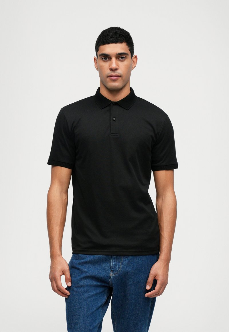 Black polo shirt made of cotton, featuring a ribbed collar, buttoned placket, and short sleeves. Worn with blue denim jeans.