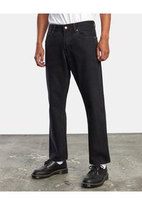 Vaqueros de mezclilla negra con un corte recto, que cuentan con cierre de botón, cinco bolsillos y costuras naranjas en contraste. Combinados con zapatos negros.