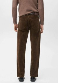 Pantalones de pana marrones con corte recto, que cuentan con dos bolsillos traseros y una superficie texturizada. Combinados con un suéter marrón de canalé y zapatos negros.