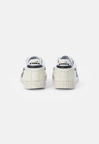 Zapatillas blancas y marinas con un acabado texturizado. Presentan un cuello acolchado y suela de goma con dibujo visible. Branding en el talón trasero.