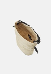Borsa beige con una texture morbida e una superficie trapuntata, dotata di un manico intrecciato nero. L'interno è rivestito con un tessuto coordinato. Etichetta del logo discreta all'interno.