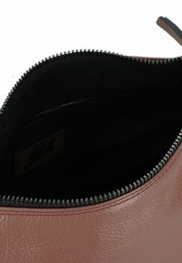 Braune Lederhandtasche mit einem schwarzen Innenfutter, ausgestattet mit einem silbernen Reißverschluss entlang der oberen Öffnung und einer glatten Oberfläche.