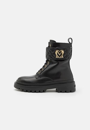 Sorte ankelstøvler i læder med en quiltet sort rem med et gyldent "M"-logo, gyldne maljer og en kraftig gummisål.