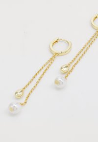 Boucles d'oreilles en or en forme de créole avec des chaînes délicates. Deux pendentifs : une goutte d'eau en or brillant et une perle blanche. Design texturé, élégant et épuré.