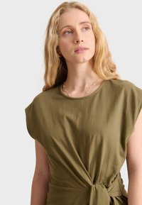 Abito verde oliva, a maniche corte, con scollatura rotonda e dettaglio annodato in vita, realizzato in tessuto morbido e leggero.