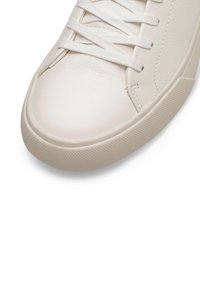 Valge nahast tennisets, lamekummiga ja ümarate varvastega, tekstuuriga beež kummitald. Puhtad jooned minimaalse õmbluse ja aktsentidega.