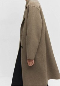 Cappotto in lana marrone con una vestibilità comoda, ampi revers e tre bottoni. Il tessuto ha una consistenza morbida e un design pulito e minimalista.