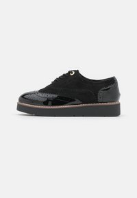 Scarpa nera stringata con punte in pelle lucida e tomaia in suede. Presenta dettagli perforati e una spessa suola in gomma nera con un bordo a contrasto.