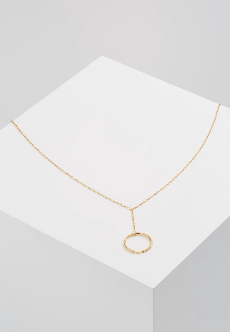 Collier délicat en chaîne d'or avec un pendentif circulaire simple, présenté sur un piédestal géométrique blanc.