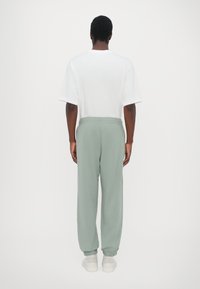 Bijela majica s kratkim rukavima i svijetlozelene trenirke, s elastičnim pojasom i manžetama, koja ima opušteni kroj i minimalistički dizajn.