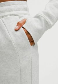 Heled hallid dressipüksid pehme tekstuuriga, külgtaskute ja soonikkoes vööni. Käsi taskus näitab detaile.