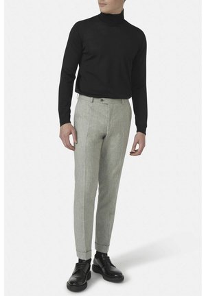 Maglione nero a collo alto abbinato a pantaloni grigi chiari su misura. I pantaloni presentano un tessuto testurizzato e una vestibilità slim, completati da scarpe nere.