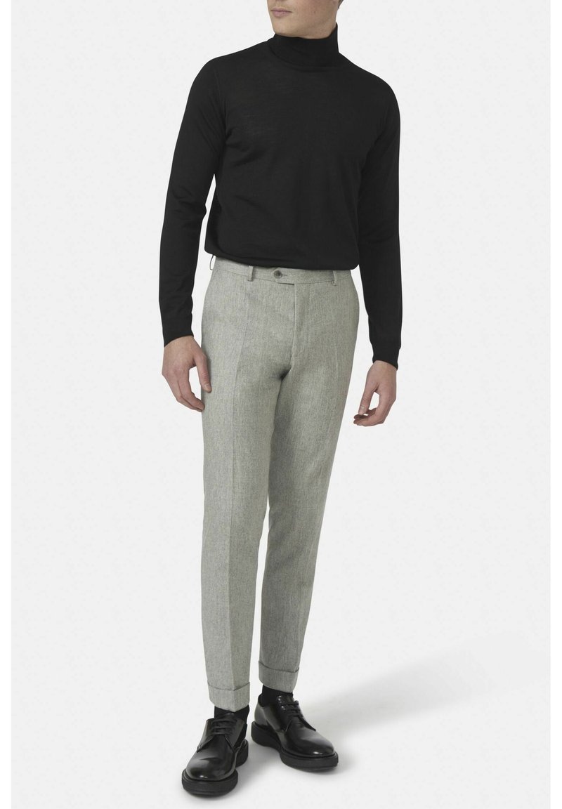 Maglione nero a collo alto abbinato a pantaloni grigi chiari su misura. I pantaloni presentano un tessuto testurizzato e una vestibilità slim, completati da scarpe nere.